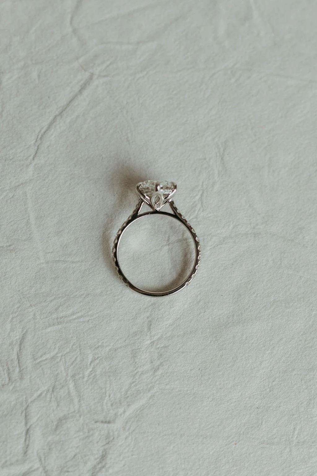 Close-up image of a silver engagement ring with a large central diamond on a light textured background.