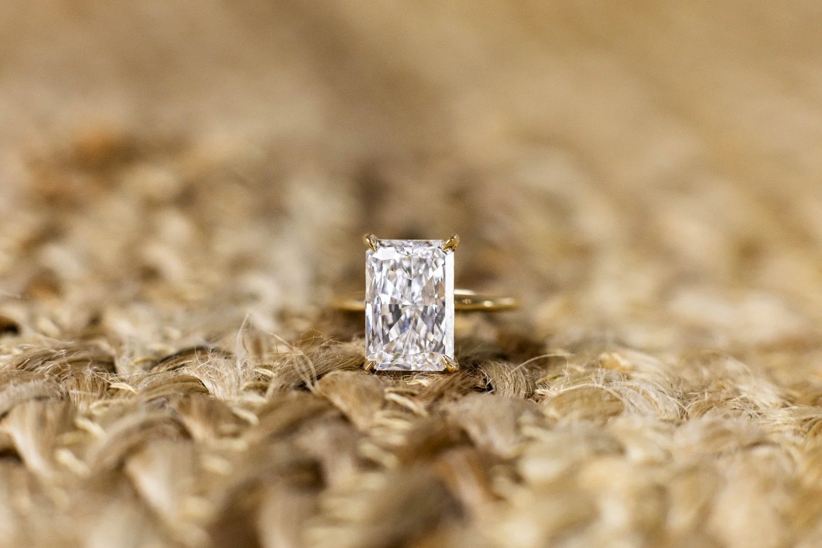 A gold ring with a large rectangular clear gemstone, possibly a diamond, resting on a textured beige surface.