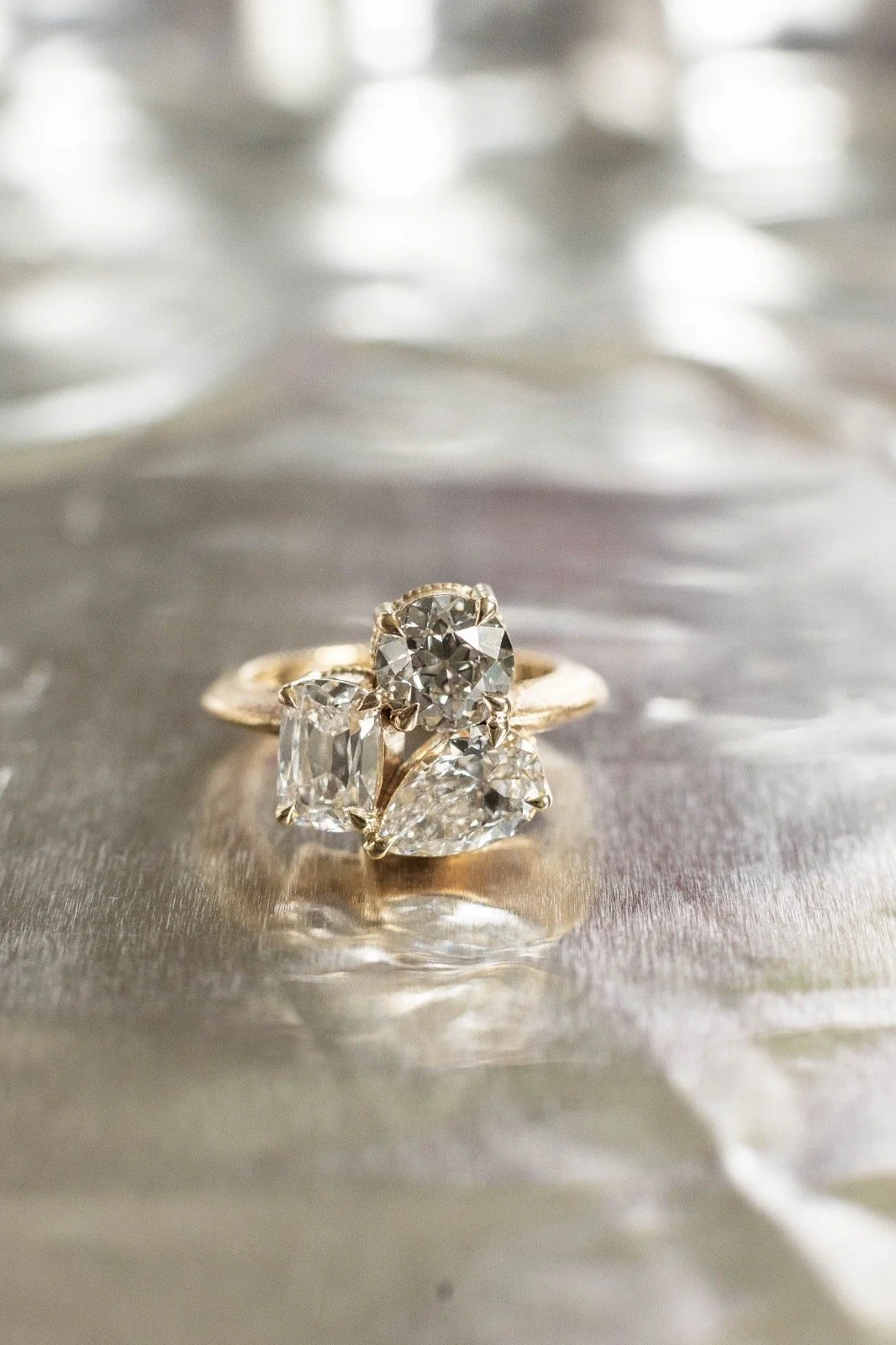 Close-up of a gold ring with multiple diamonds, resting on a reflective, textured surface with soft lighting.