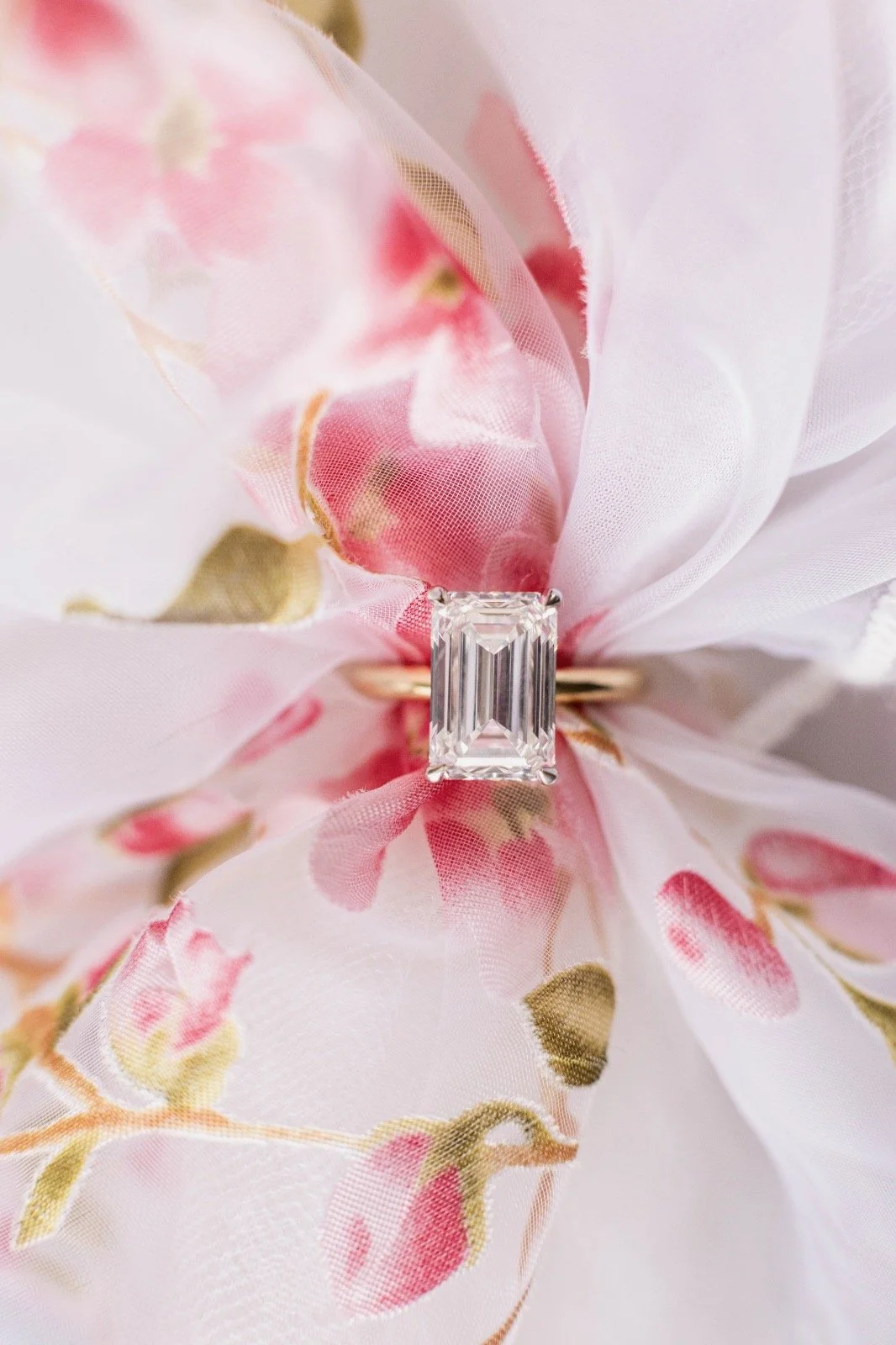 A clear rectangular cut diamond ring placed on pink and white floral-patterned fabric.