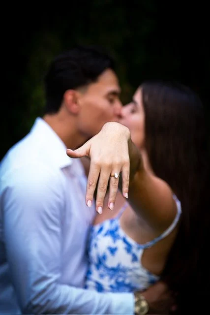 A couple kissing, with the woman showing off an engagement ring on her finger.