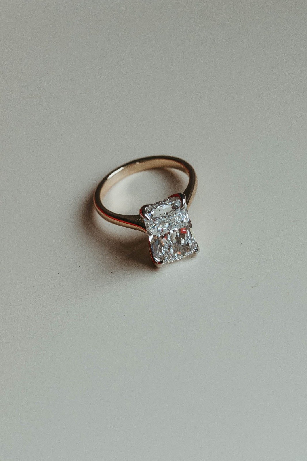 A gold ring with a large rectangular clear gemstone, likely a diamond, set on a white surface.