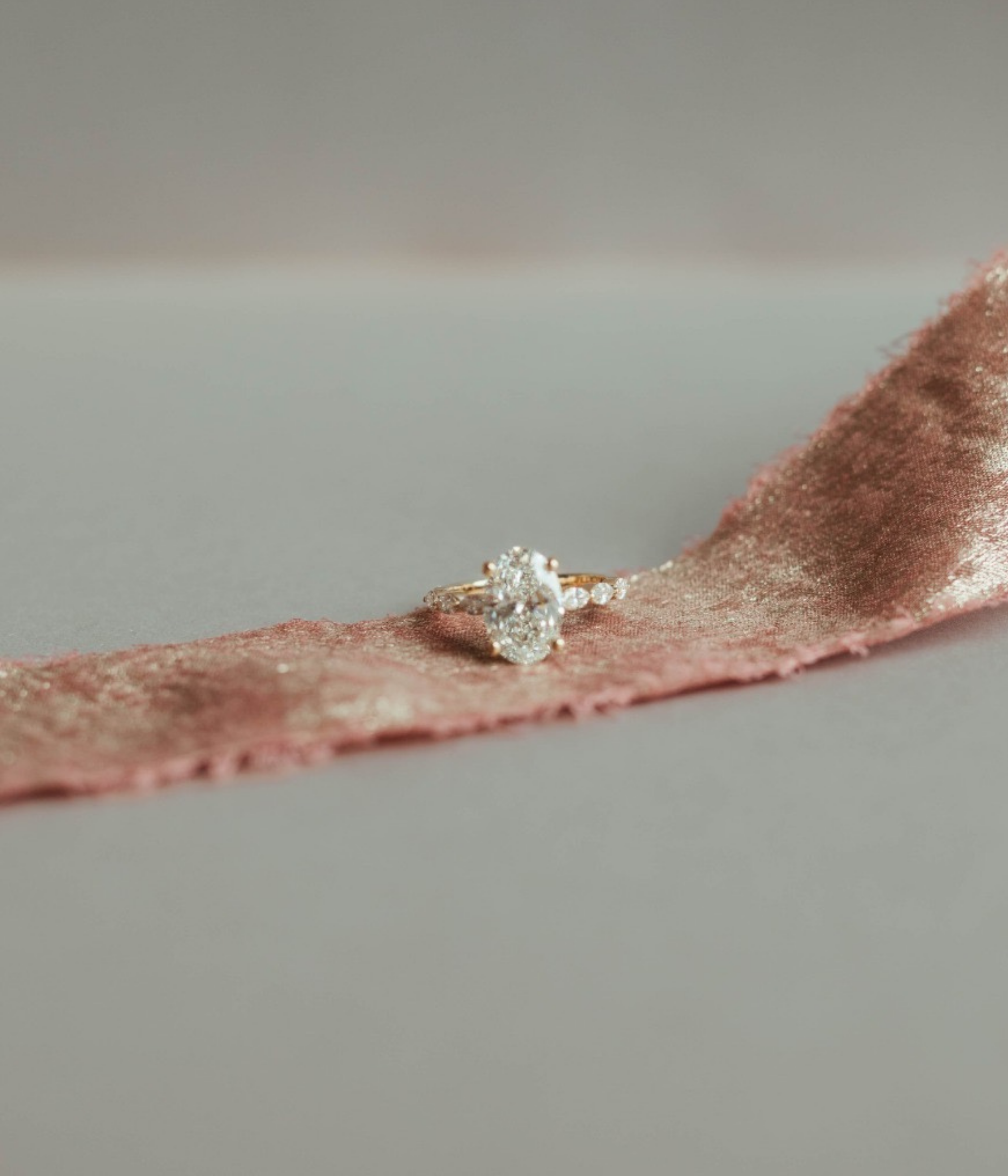 Close-up of a diamond engagement ring with a pink fabric backdrop.