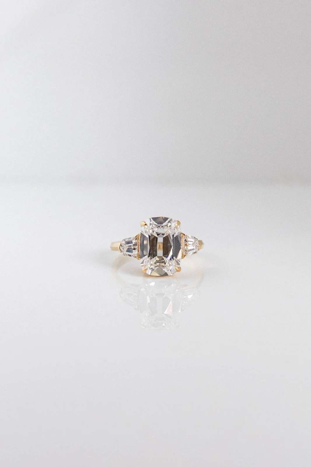 Jewelry ring with a large central diamond and smaller side diamonds on a reflective surface