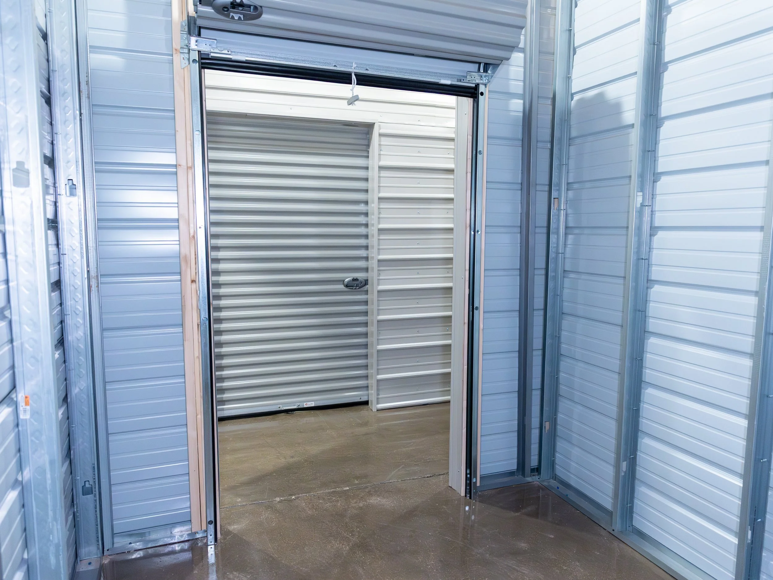 Interior of a storage unit or garage with aluminum walls and an open garage door leading to a concrete floor.