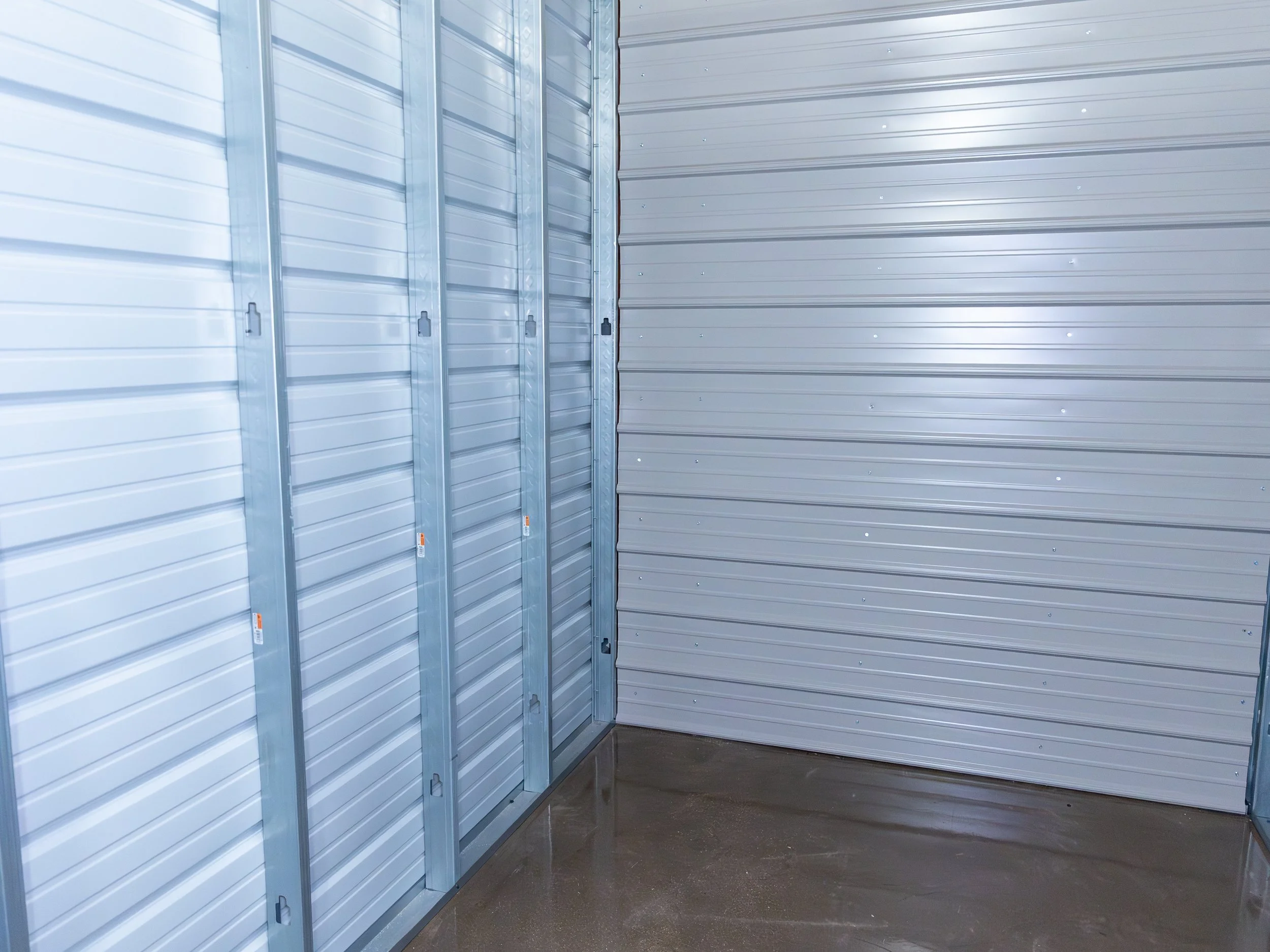 Interior of a storage unit with metal walls and a concrete floor, empty and well-lit.
