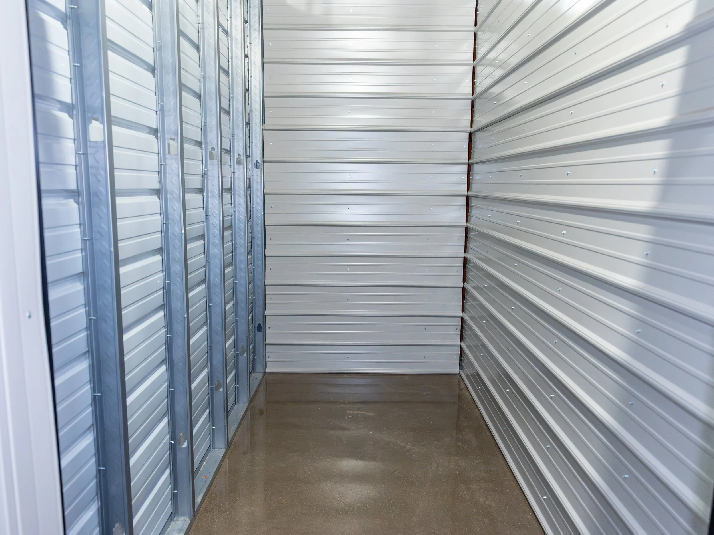 Interior of a storage unit with metal walls and a shiny concrete floor.