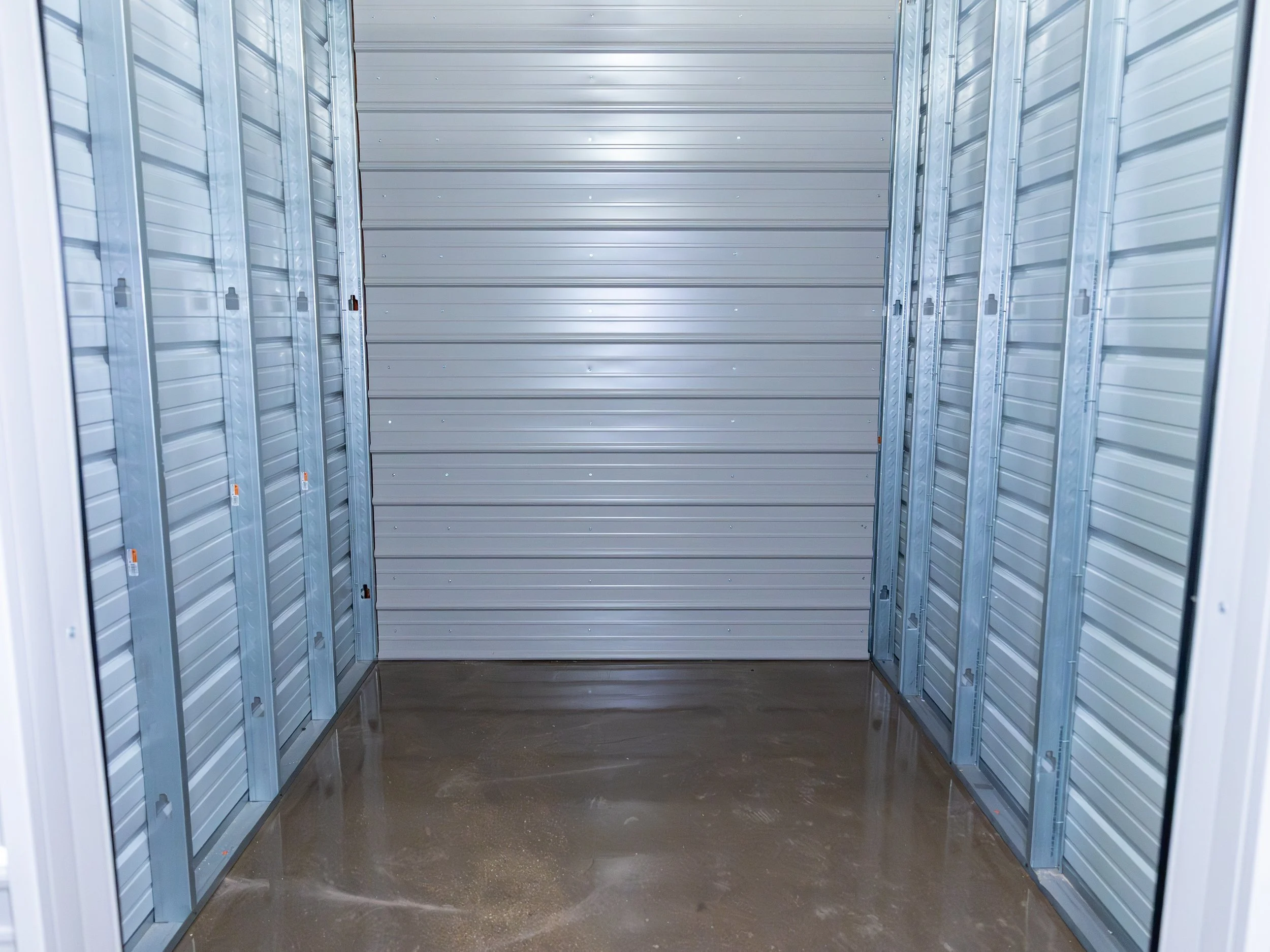 Empty storage unit with metal walls and a concrete floor.