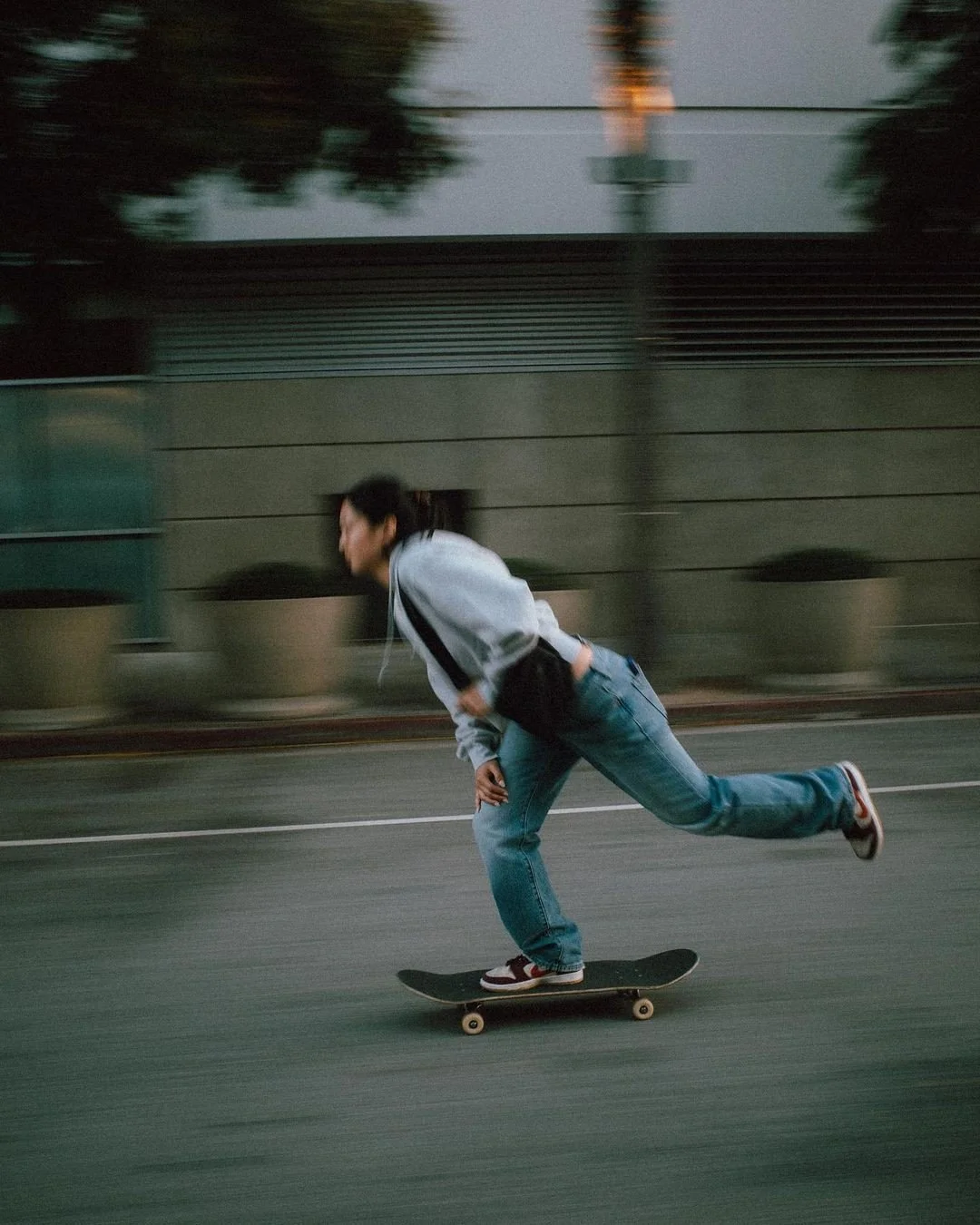 Person skateboarding on the street during dusk or evening in an urban area.