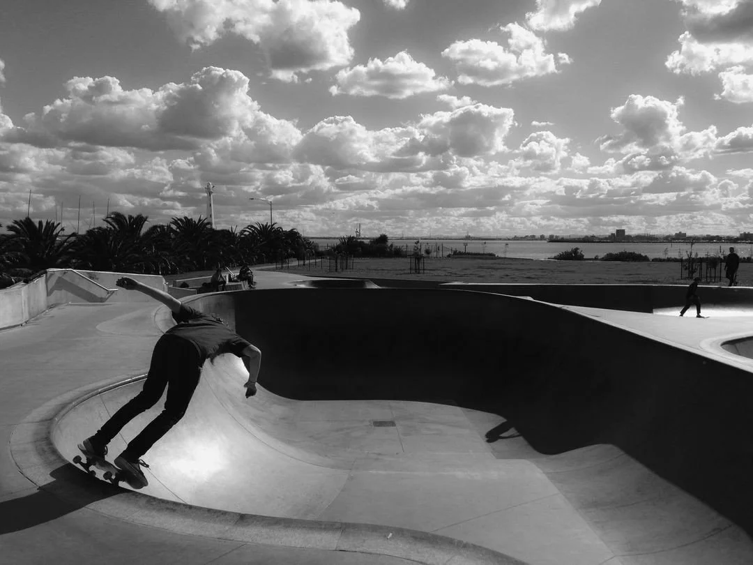 Skateboarder performing a trick in a skatepark with a cloudy sky and trees in the background.