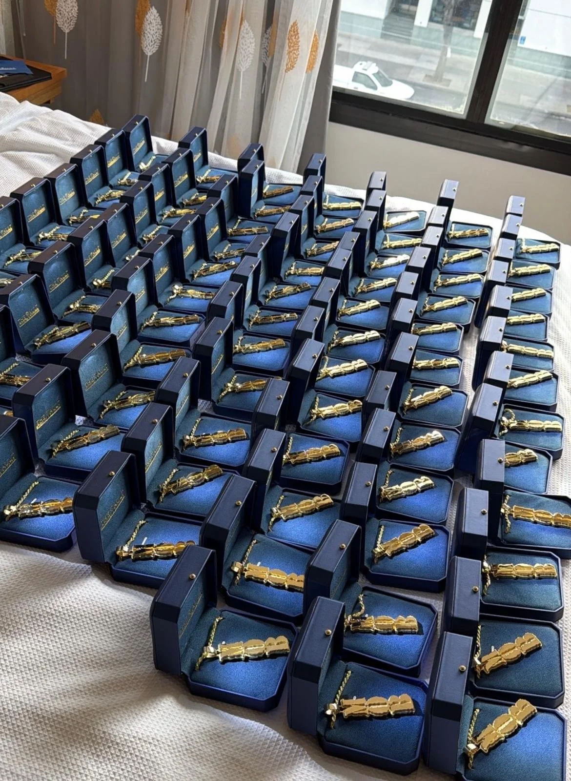 Numerous gold-colored necklaces displayed in open blue boxes on a table, arranged in rows. For Seahawks Football team for Superbowl 