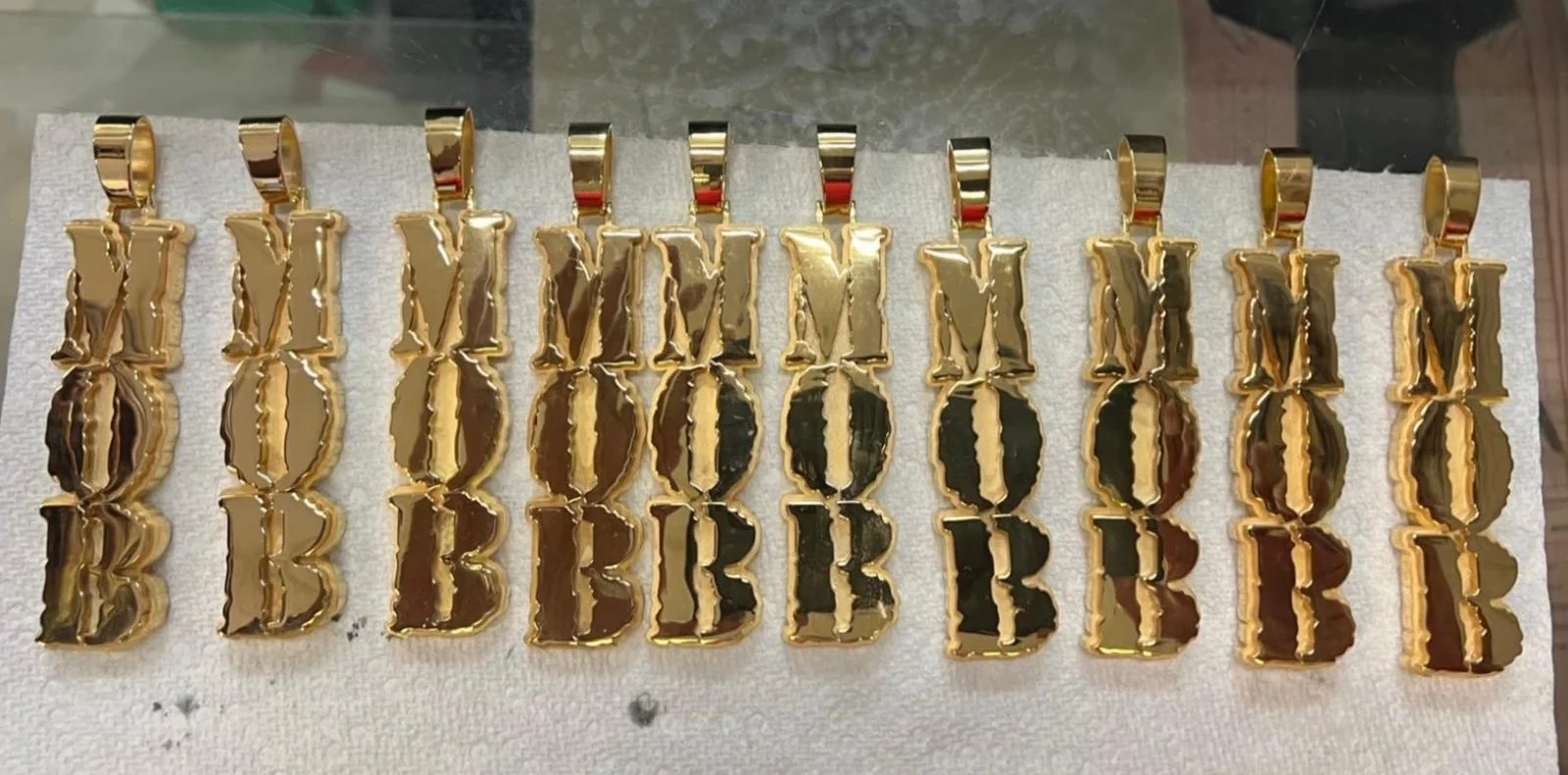 Gold-colored metallic 'MOB' pendant charms arranged on a white towel. Designed for the seahawks football team for Superbowl