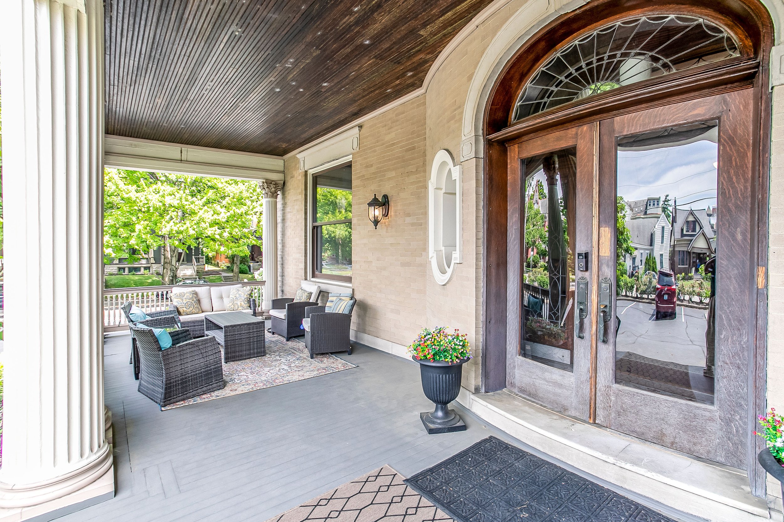 Covered porch with wicker furniture, a rug, a flower pot, and a glass door reflecting the street view.