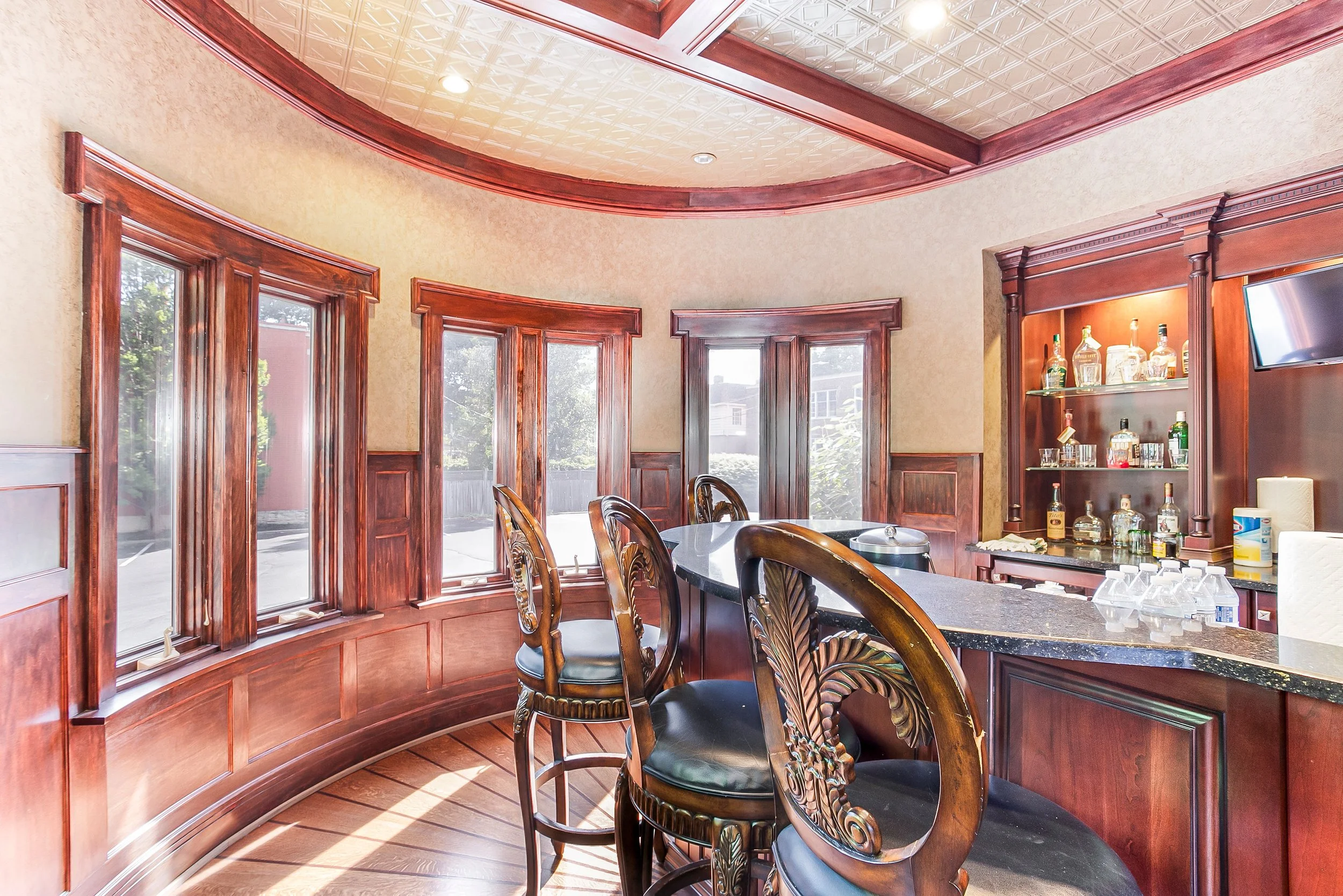 Bar with wooden chairs, windows, and liquor bottles display