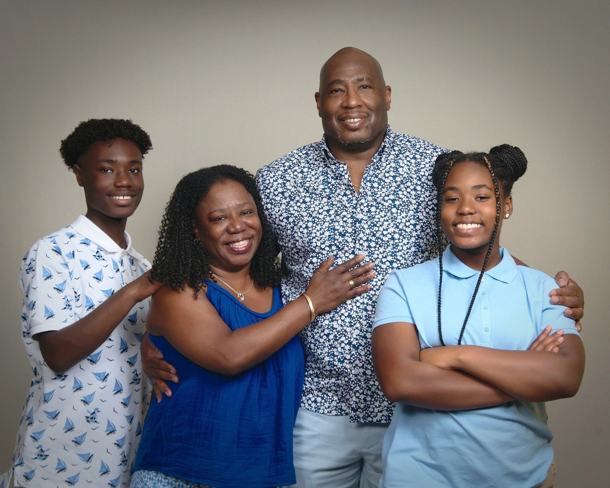 A family of five smiling and posing together against a plain beige background, with two young girls, a woman, a man, and another young girl.