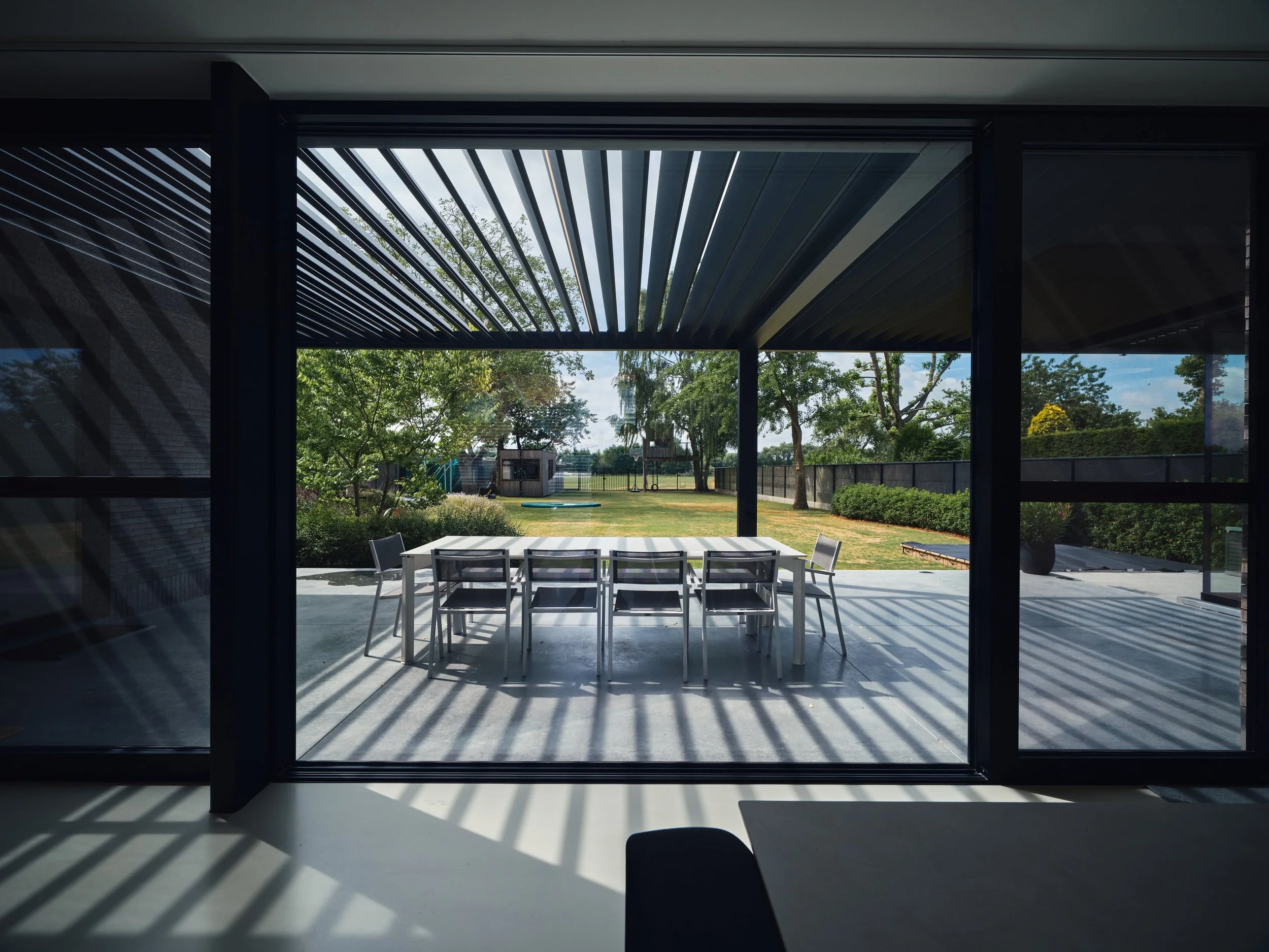 Uitzicht vanuit de leefruimte op een zwart Renson lamellendak, type Algarve, geplaatst te Kalfort, Antwerpen door Leroy-Alu