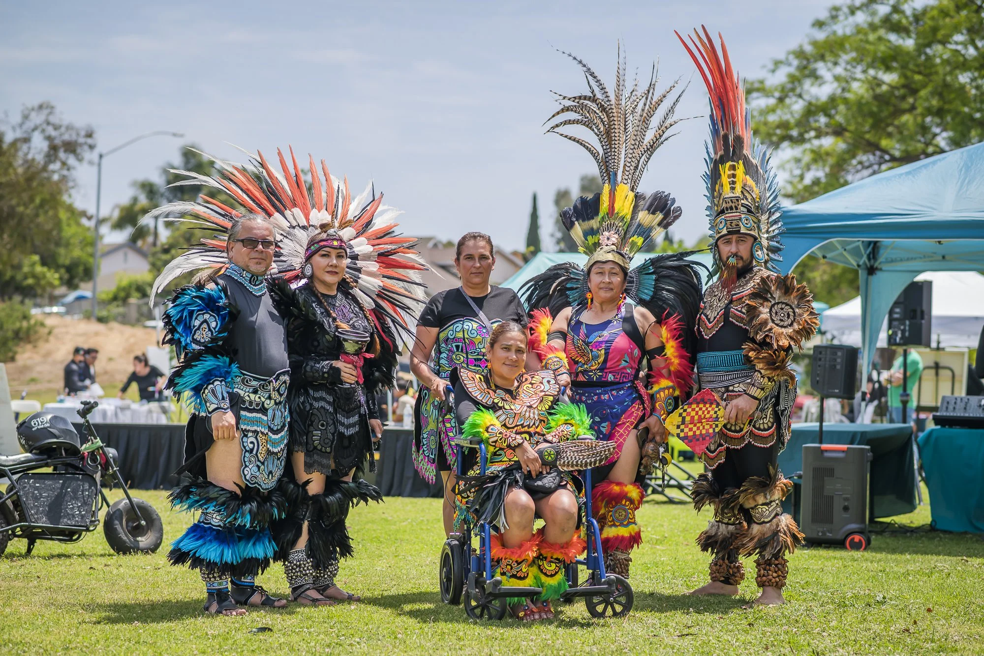 Group of people dressed in traditional Native American costumes with feathered headdresses at an outdoor event.