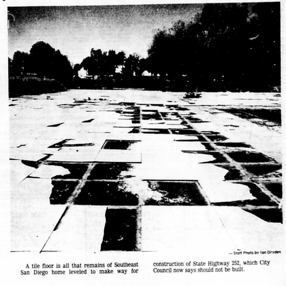 Black and white photograph of a broken tile floor on a street, with trees in the background. The caption mentions it is the remains of a Southeast San Diego home that was leveled to create space for a proposed highway, which the city council now says should not be built.