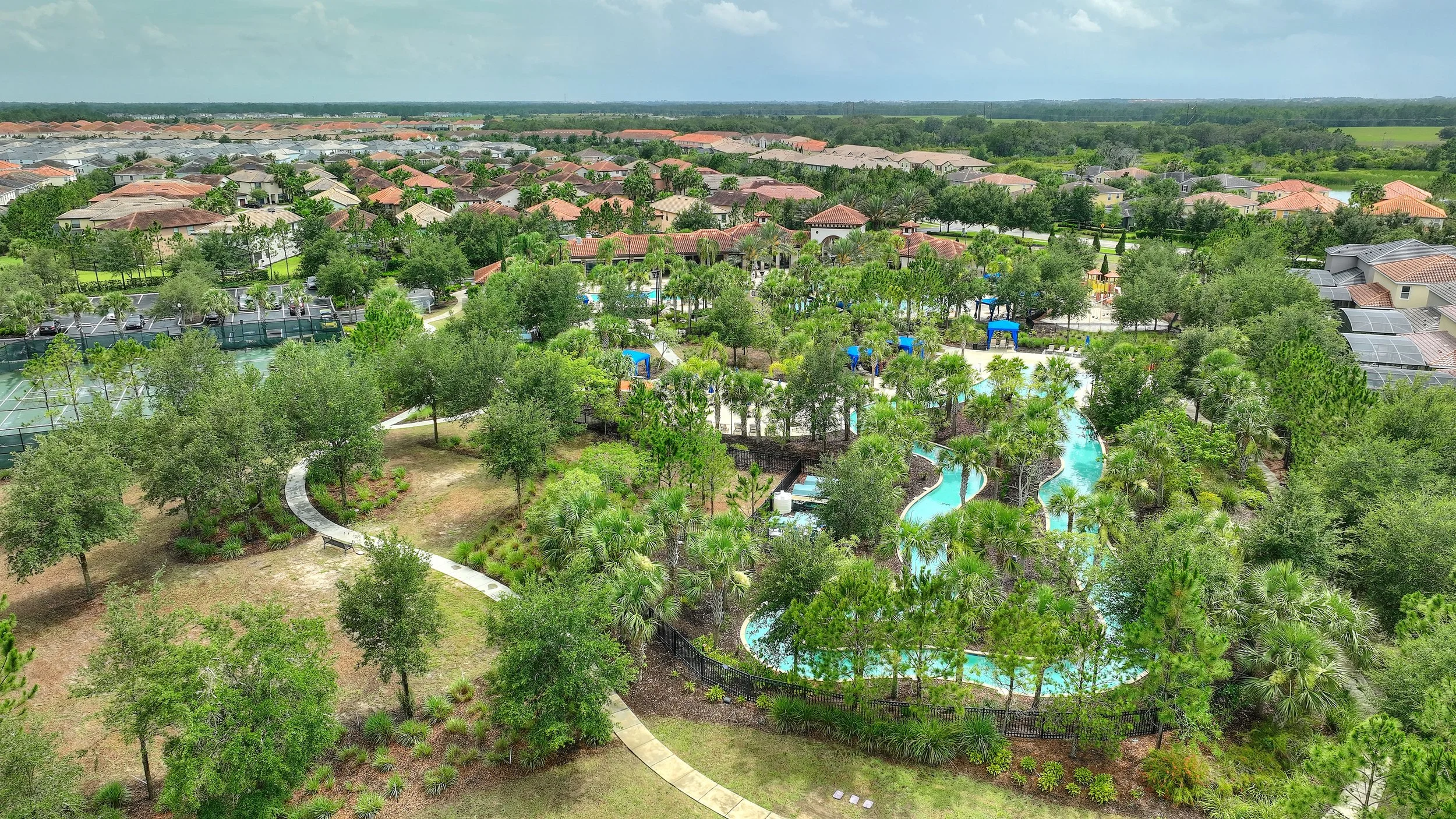 Aerial view of a neighborhood with a community swimming pool, surrounding greenery, and houses with red-tiled roofs.