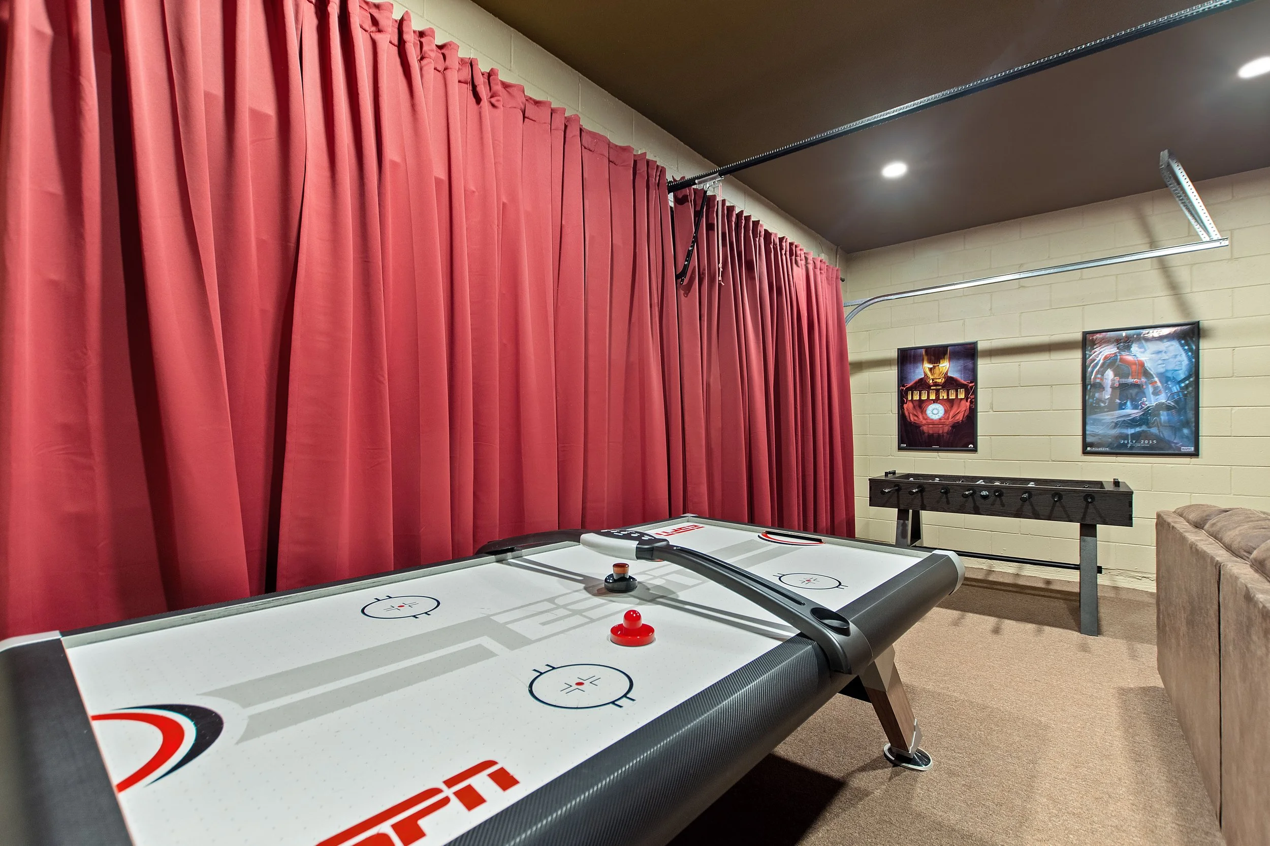 Indoor recreation room featuring an air hockey table, red curtains, framed movie posters on the wall, and a foosball table.
