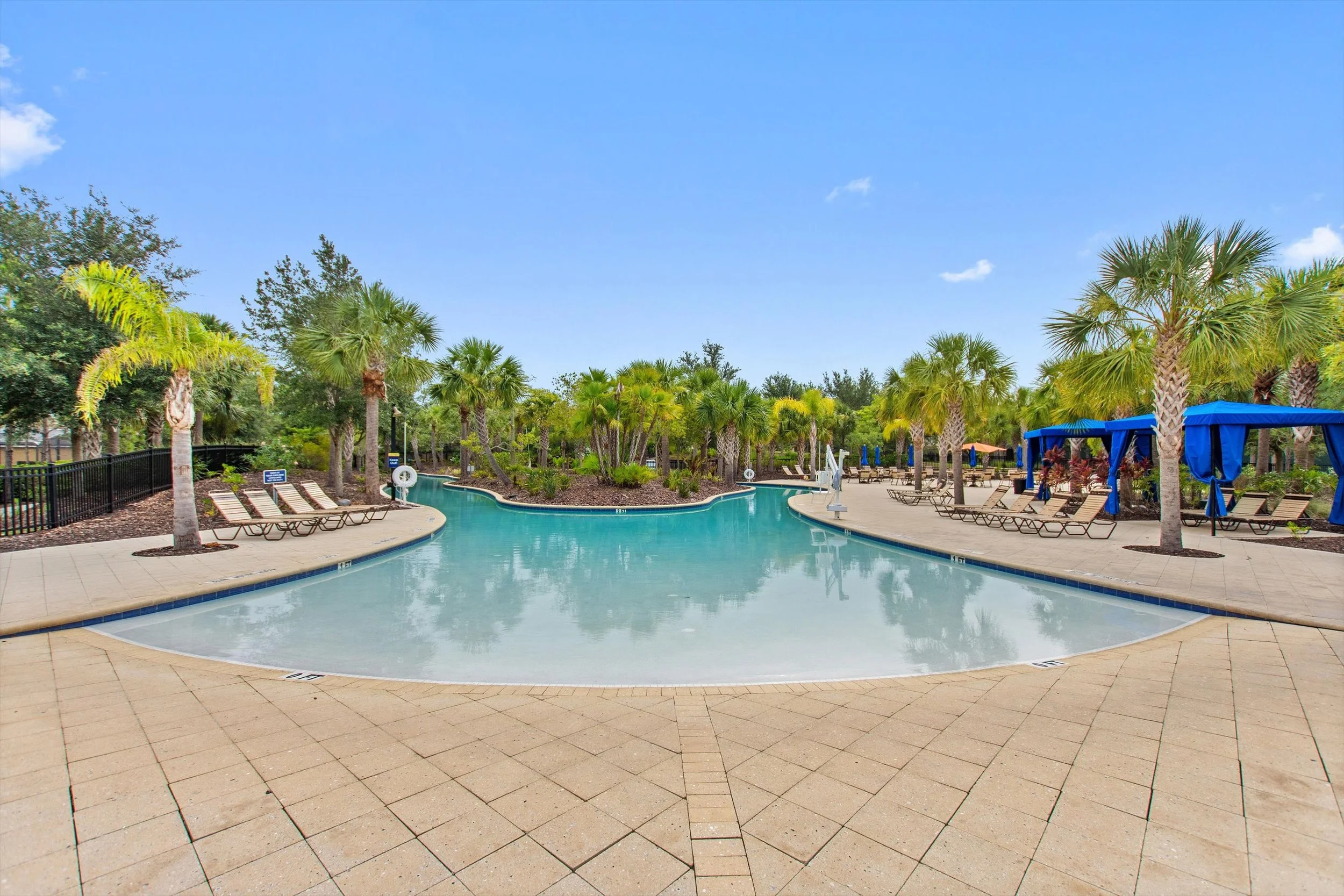 Empty swimming pool surrounded by palm trees and lounge chairs on a sunny day.