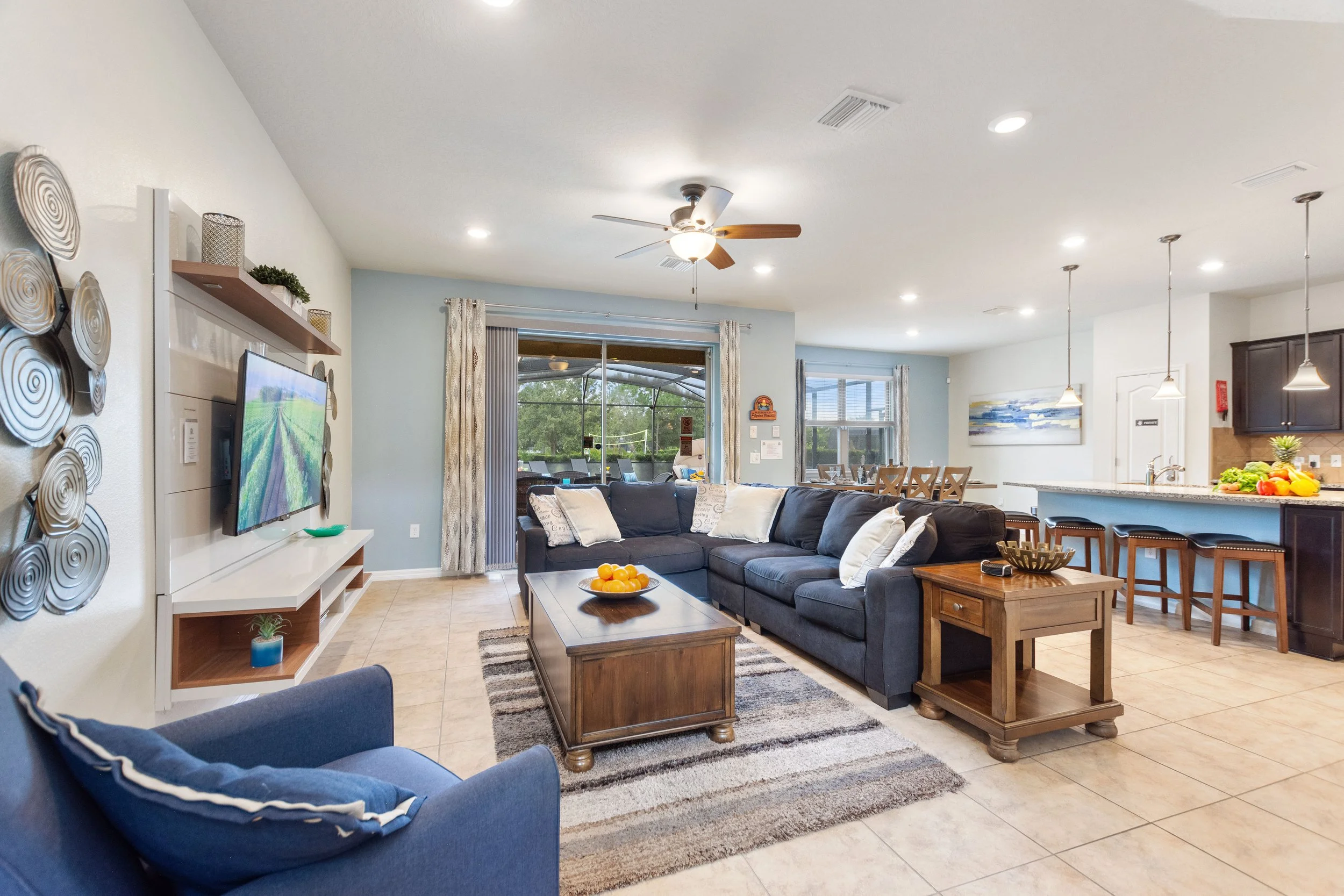 Living room with a navy couch, wooden coffee table, TV on wall, sliding glass door, and kitchen bar with stools.