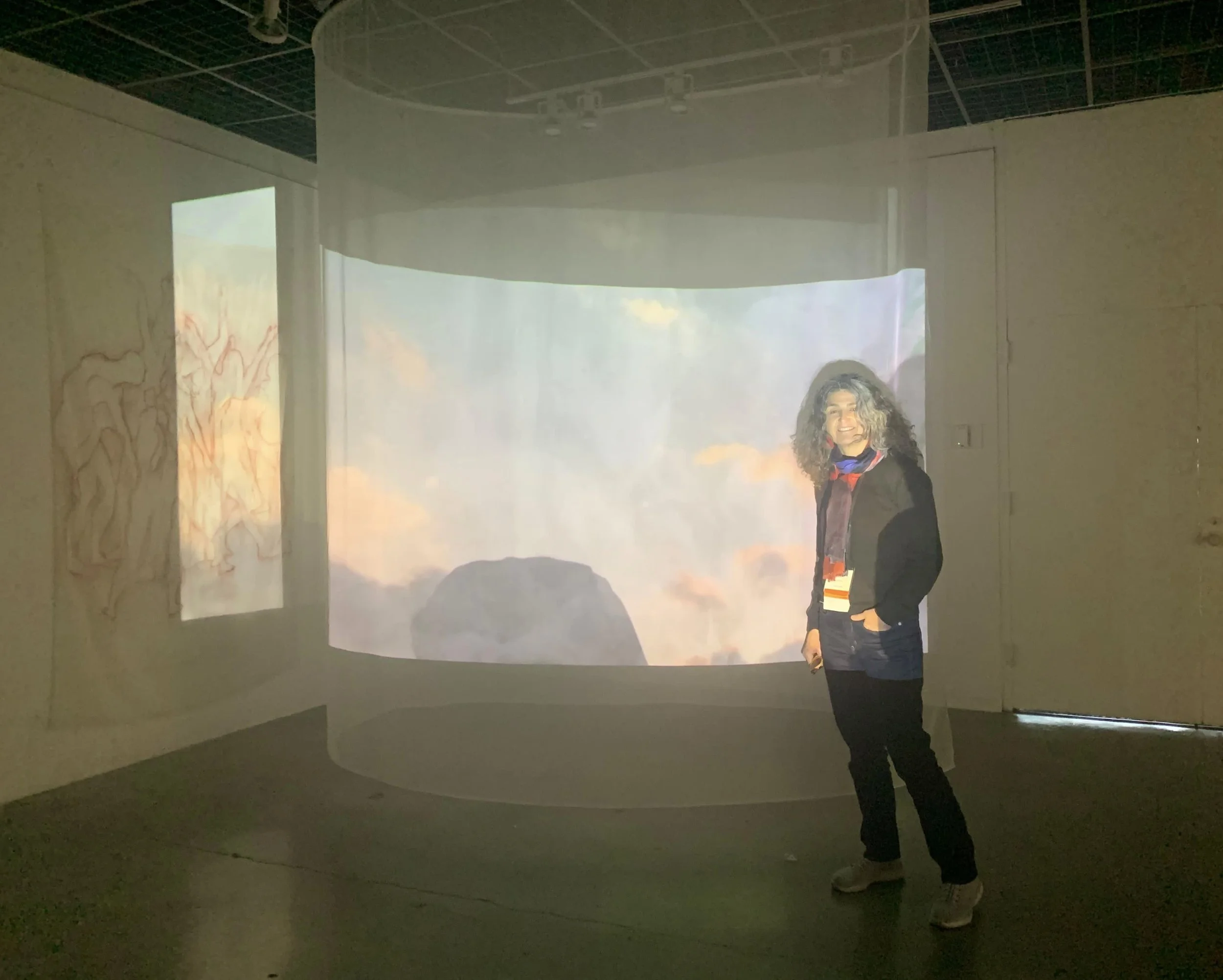 Woman standing in front of a circular projection of sky and clouds inside an art exhibit.