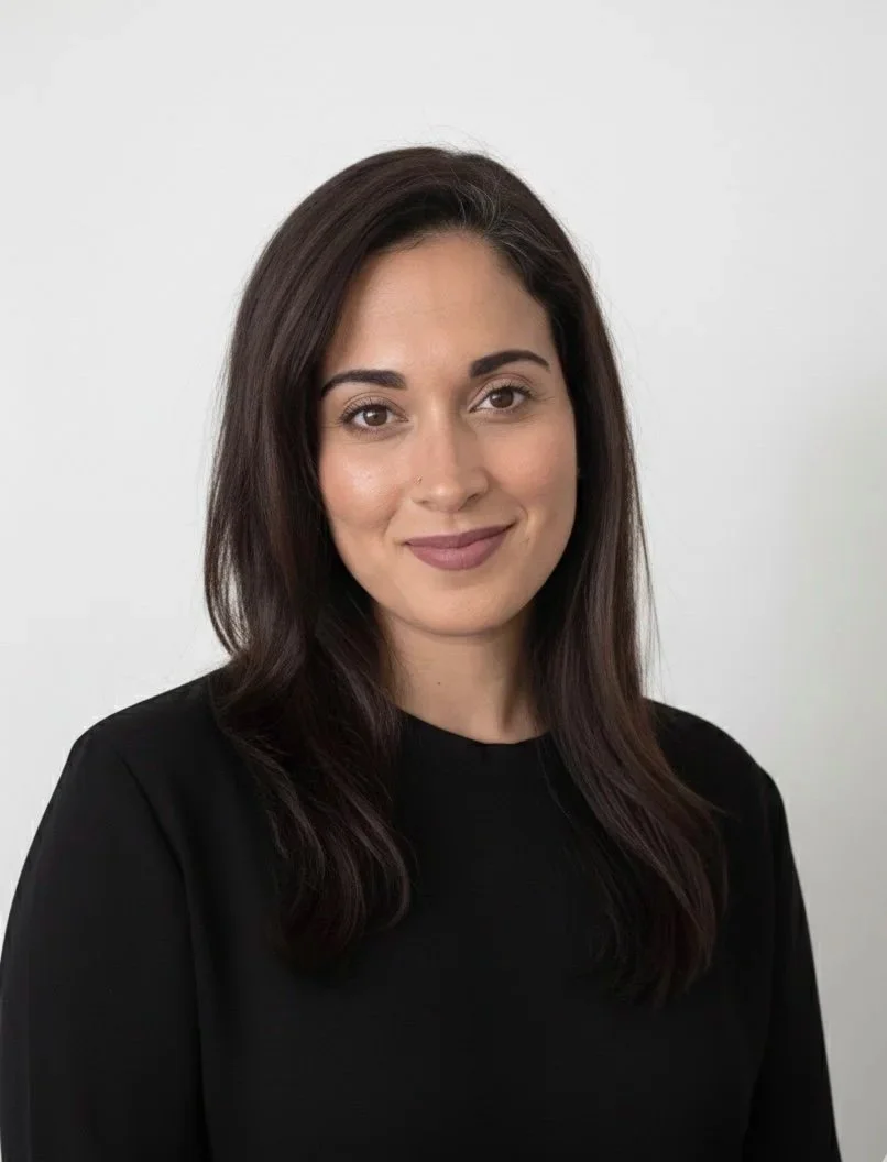 Portrait of a young woman with dark brown hair, wearing a black top, standing against a plain white background.