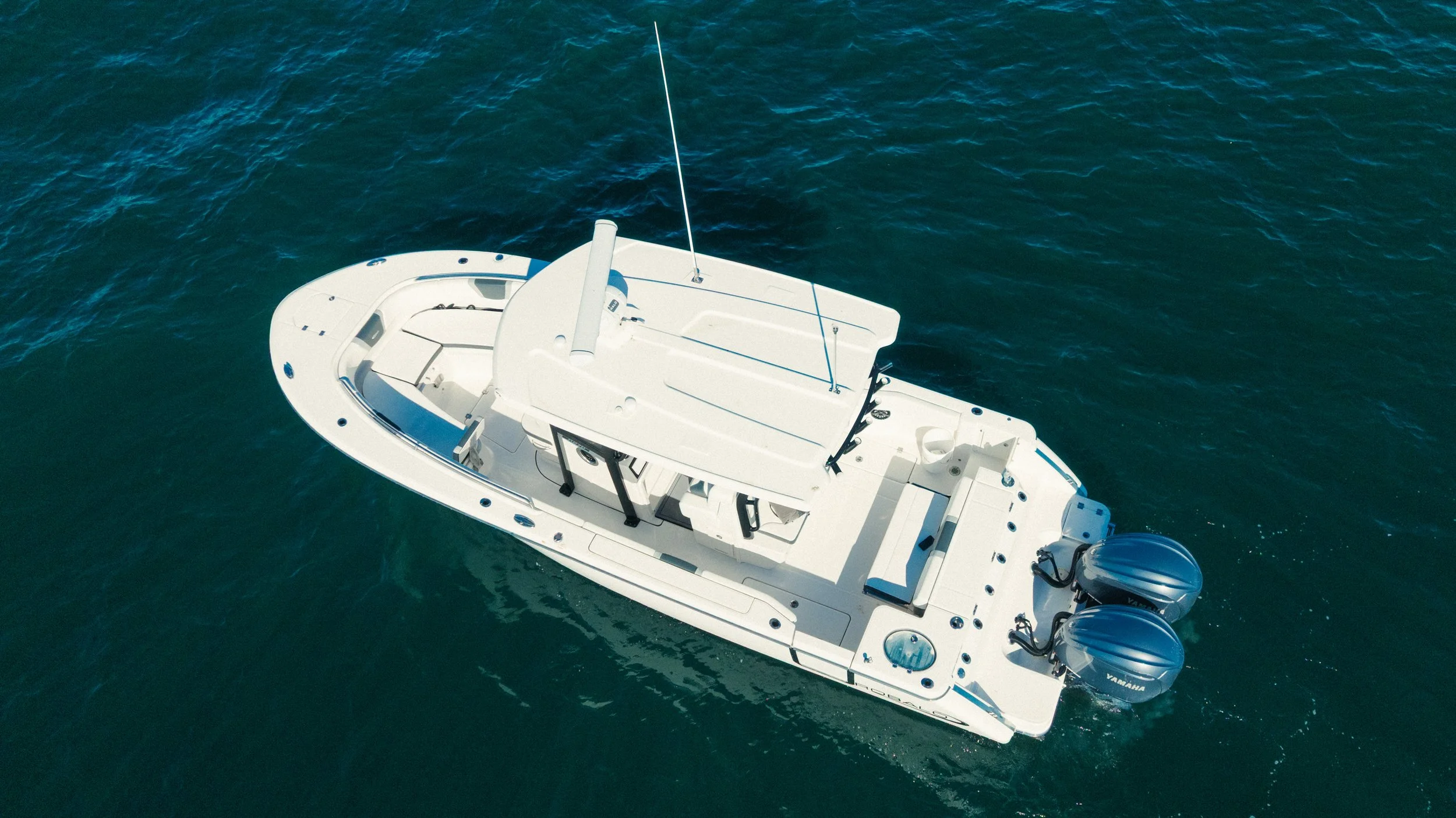 Overhead view of a white motorboat with dual outboard engines floating on dark blue water.