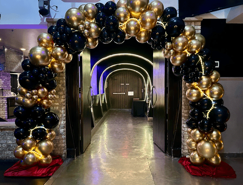 Archway decorated with black and gold balloons at an event venue.