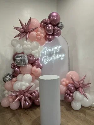 Pink, white, and metallic balloons shaped as stars and clusters, with a neon light reading 'Happy Birthday'.