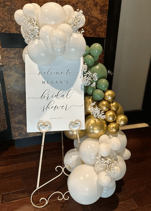 Bridal shower decoration with a white welcome sign surrounded by white, gold, and green balloons.