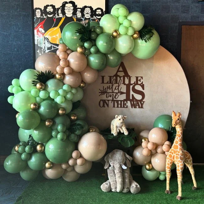 Decorative baby shower setup with balloons, stuffed animal toys, and an inspirational sign that reads "A little wild one is on the way."