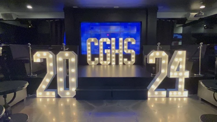Decorative illuminated number 2024 and a sign with letters CGHS on a stage for a graduation.