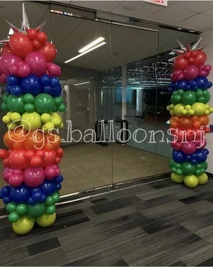 Colorful balloon columns with rainbow colors at a doorway inside a building.