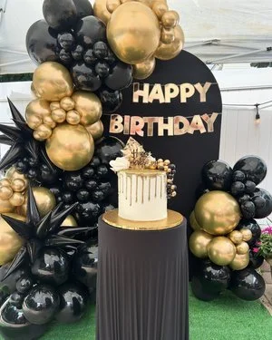 Balloon display with black, gold, and black star-shaped balloons, a round black sign reading "HAPPY BIRTHDAY".