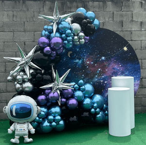 Decorative space-themed balloon arrangement with silver stars, black, purple, and blue balloons, a galaxy backdrop, and an astronaut figure.