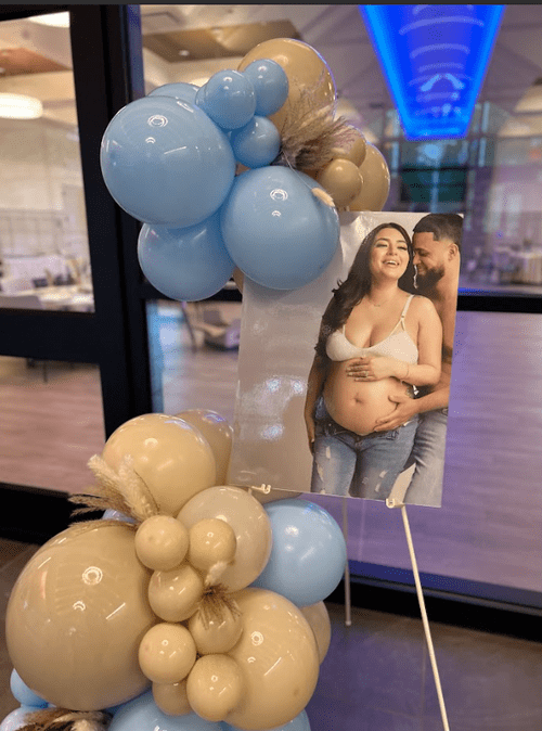 Decorative balloon arrangement with beige and blue balloons, and a photo of a pregnant woman smiling with a man.