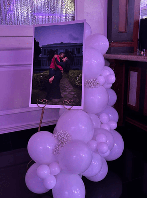 A framed photograph of a couple kissing, displayed on a stand decorated with white balloons in varying sizes.