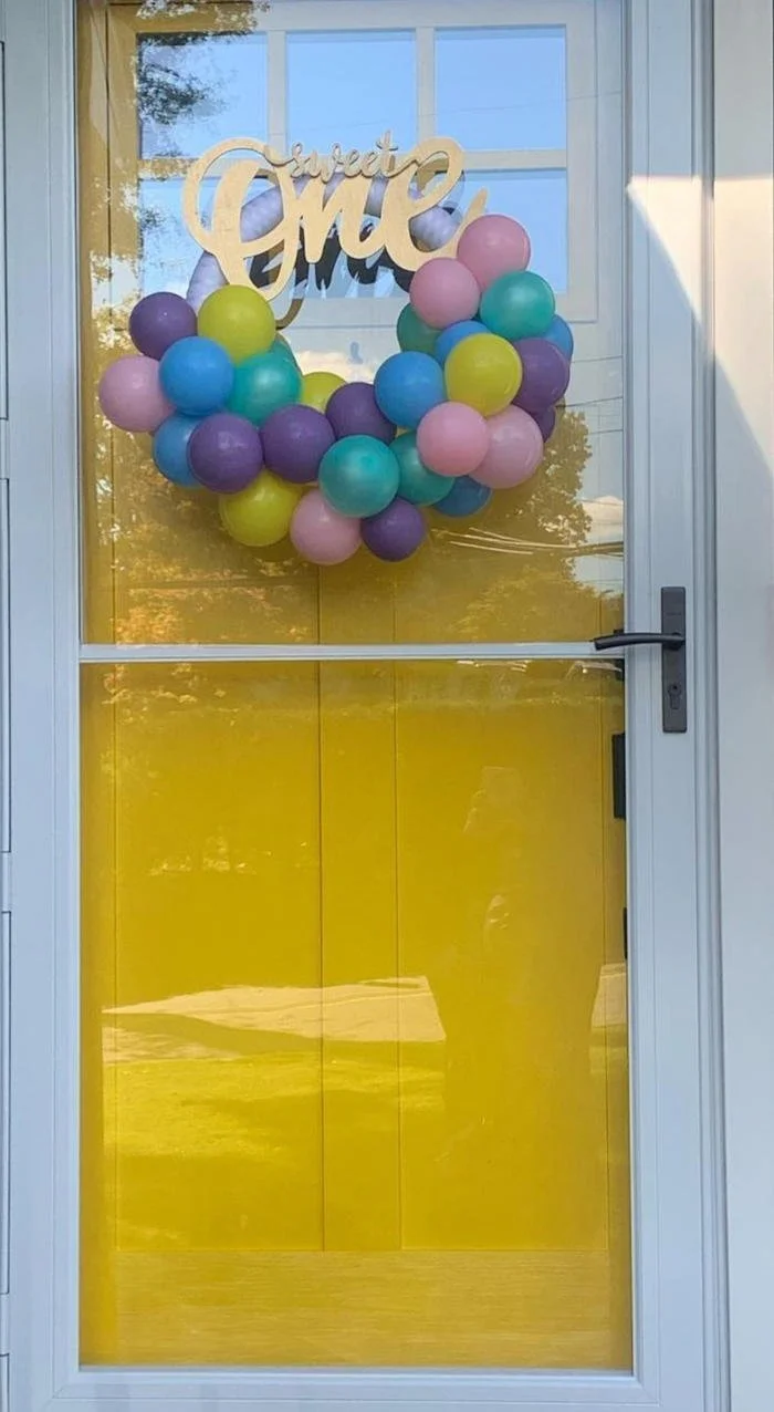 Decorative door with a balloon wreath in pastel colors and a wooden sign that says "Sweet One".
