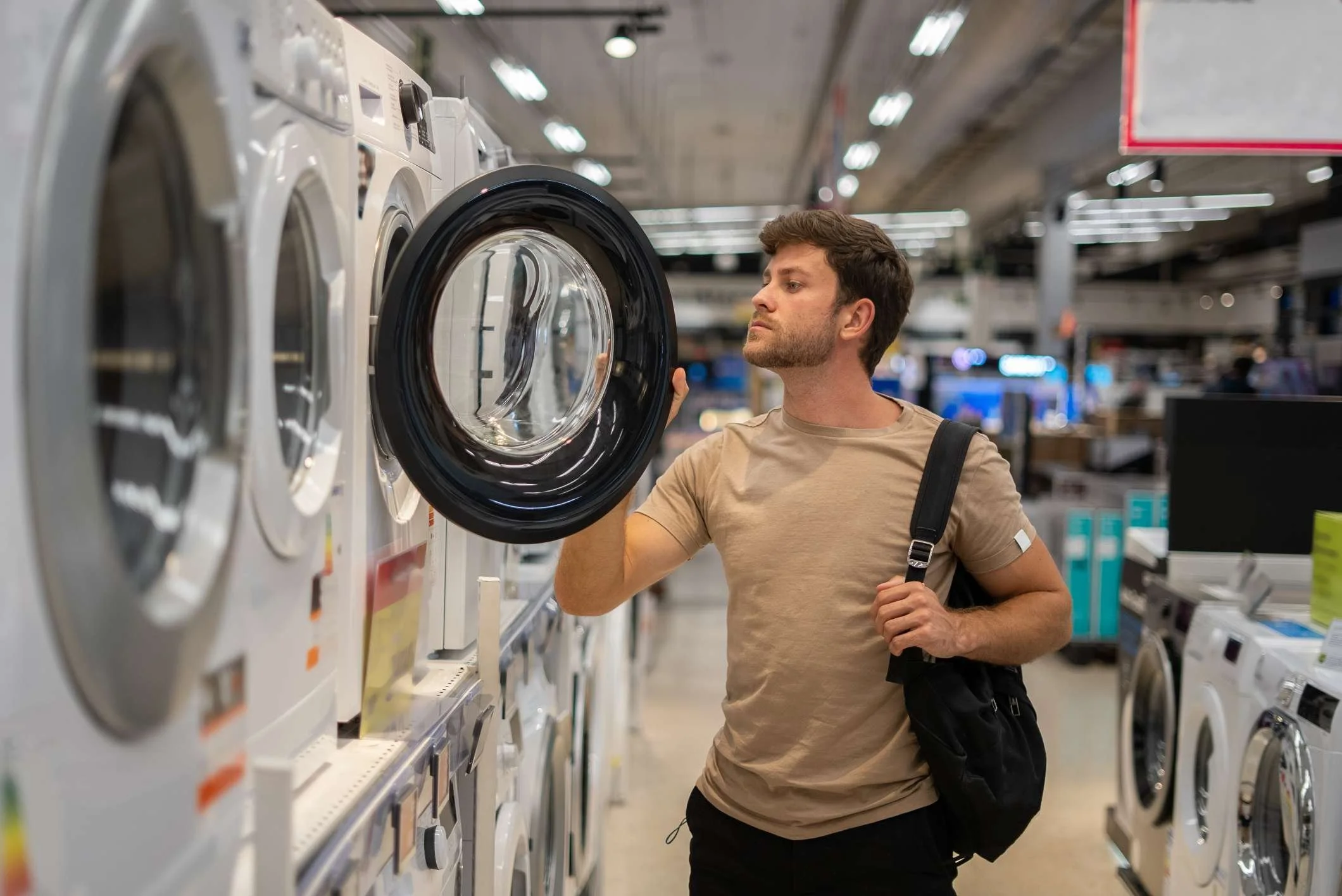 a young man with a brown shirt looking at a dryer in a appliance retail store