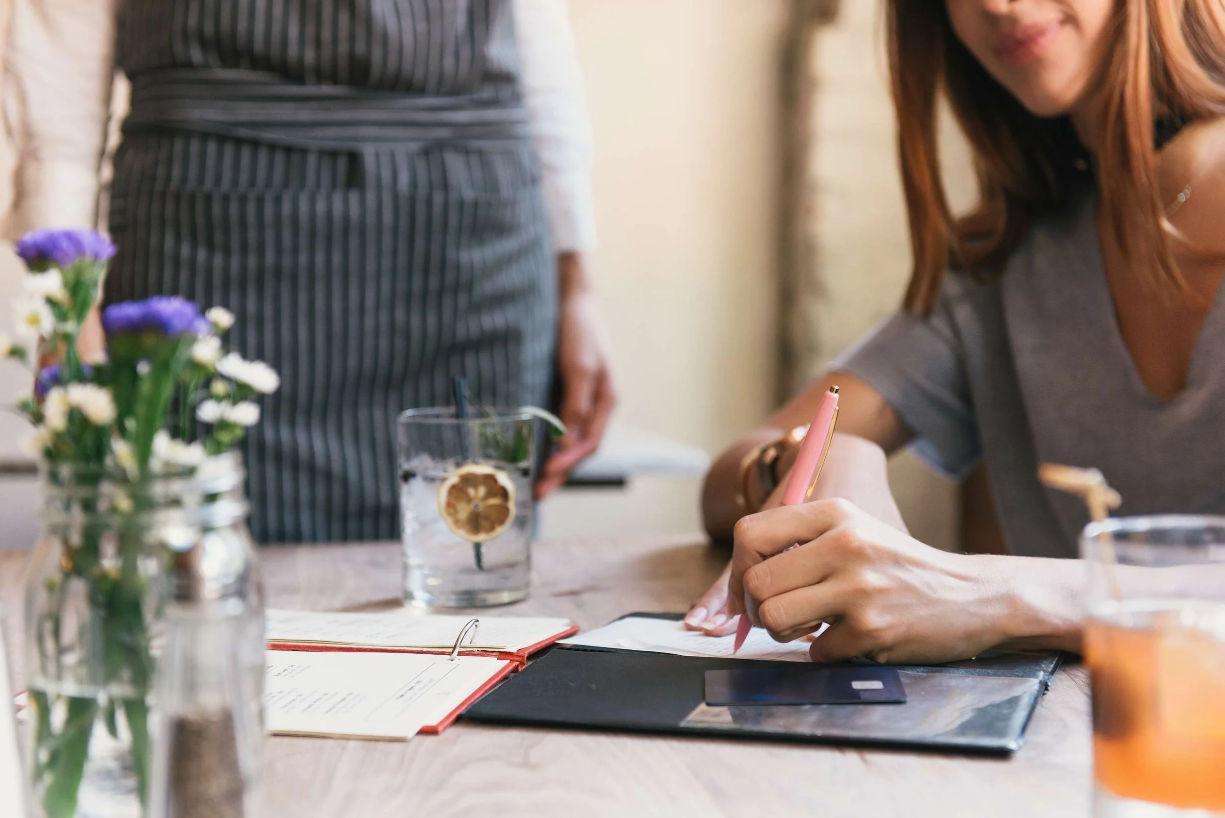 a women signing her bill at a restaurant with a peach colored pen