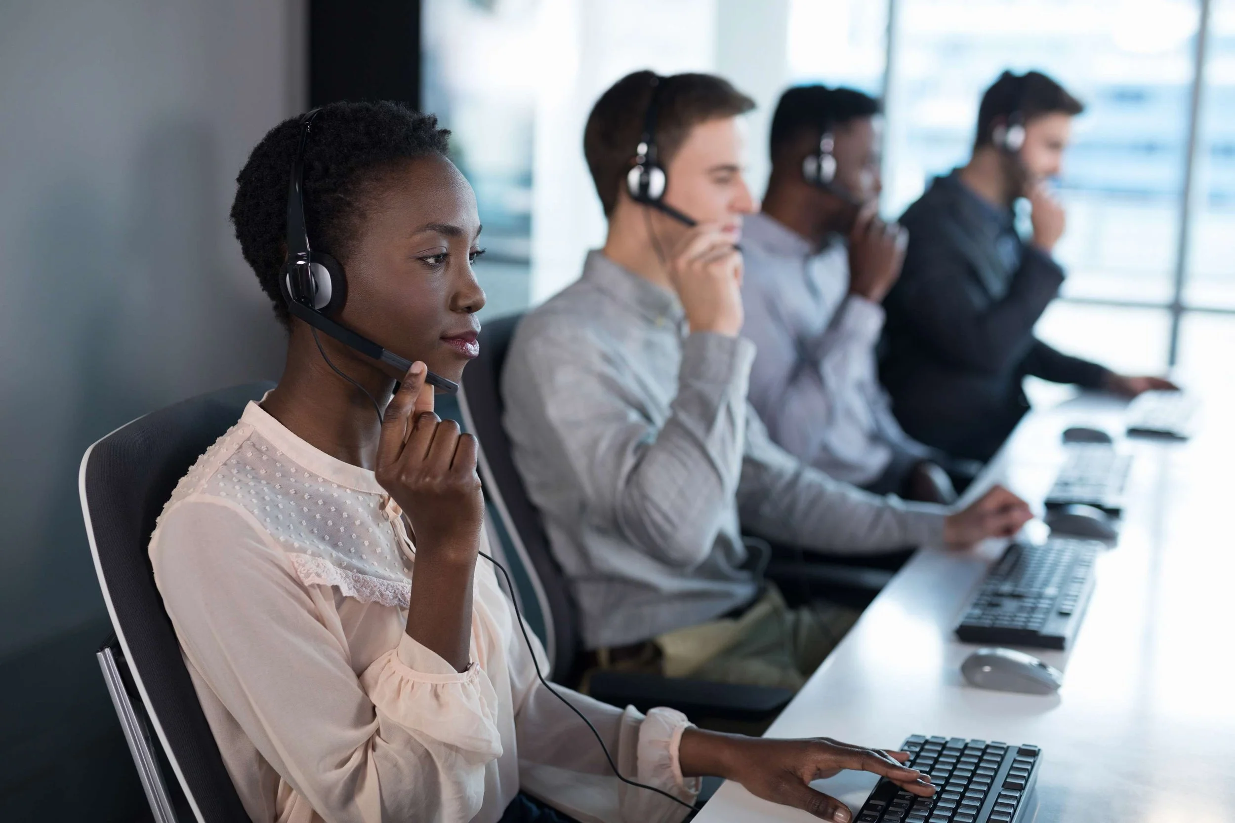 an image of a woman and three men with headsets on answering calls