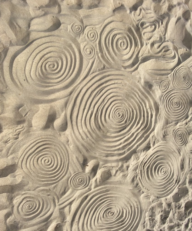 Close-up view of sand with spiral patterns carved into it.