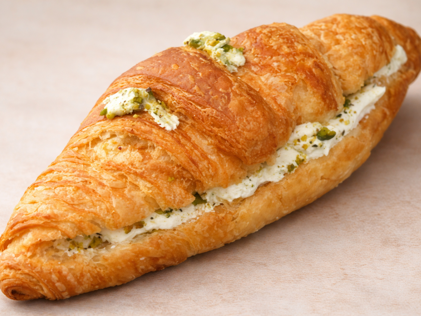 Bakery croissant filled with cream cheese and topped with chopped pistachios.