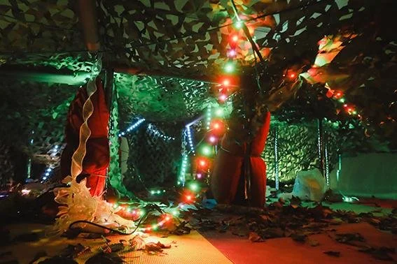 Decorated outdoor space with colorful Christmas lights, red curtains, and camouflage fabric ceiling, creating a festive atmosphere.
