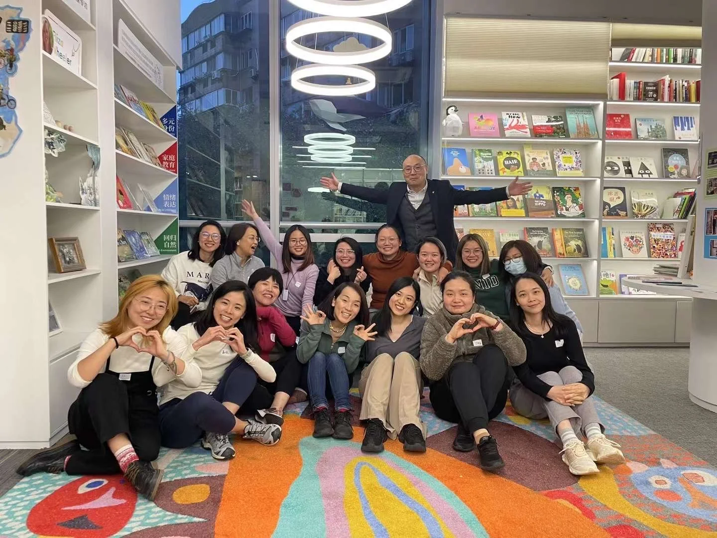 Group of people smiling and making heart shapes with their hands in a bookstore or library.