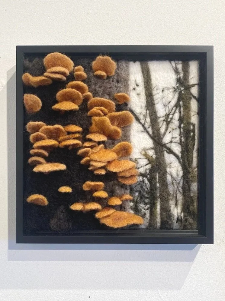 Felted artwork depicting a tree trunk and branches with orange mushrooms growing on the left side.