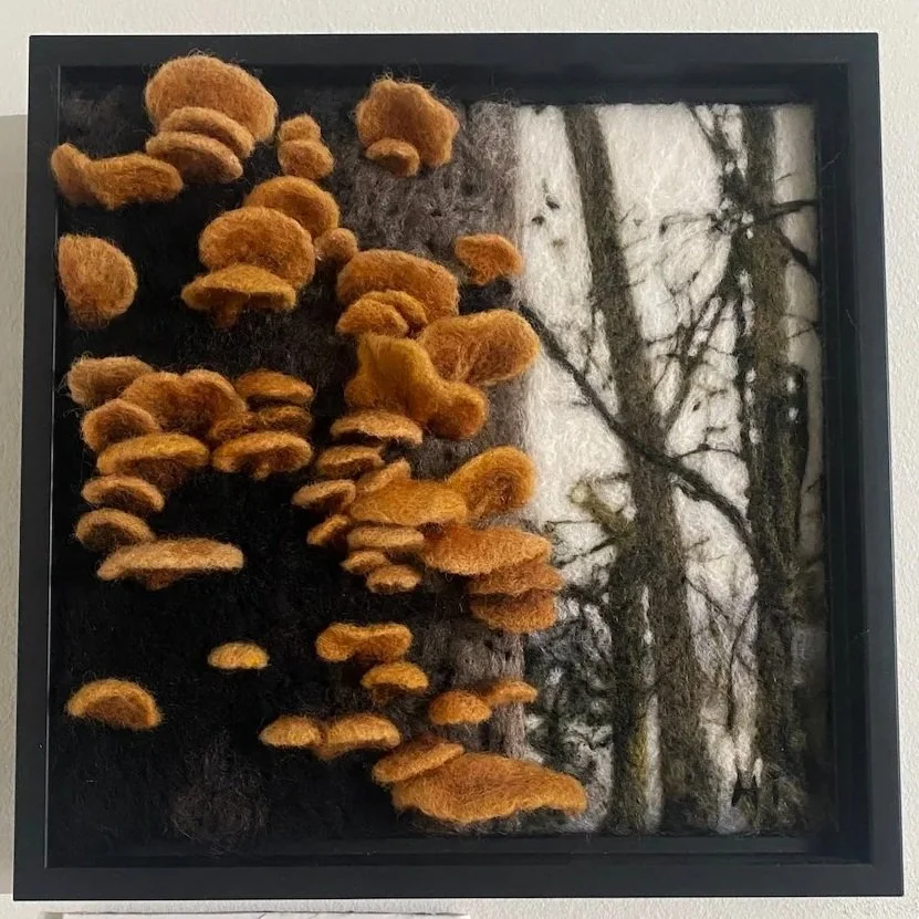 Felted artwork depicting a tree trunk and branches with orange mushrooms growing on the left side.
