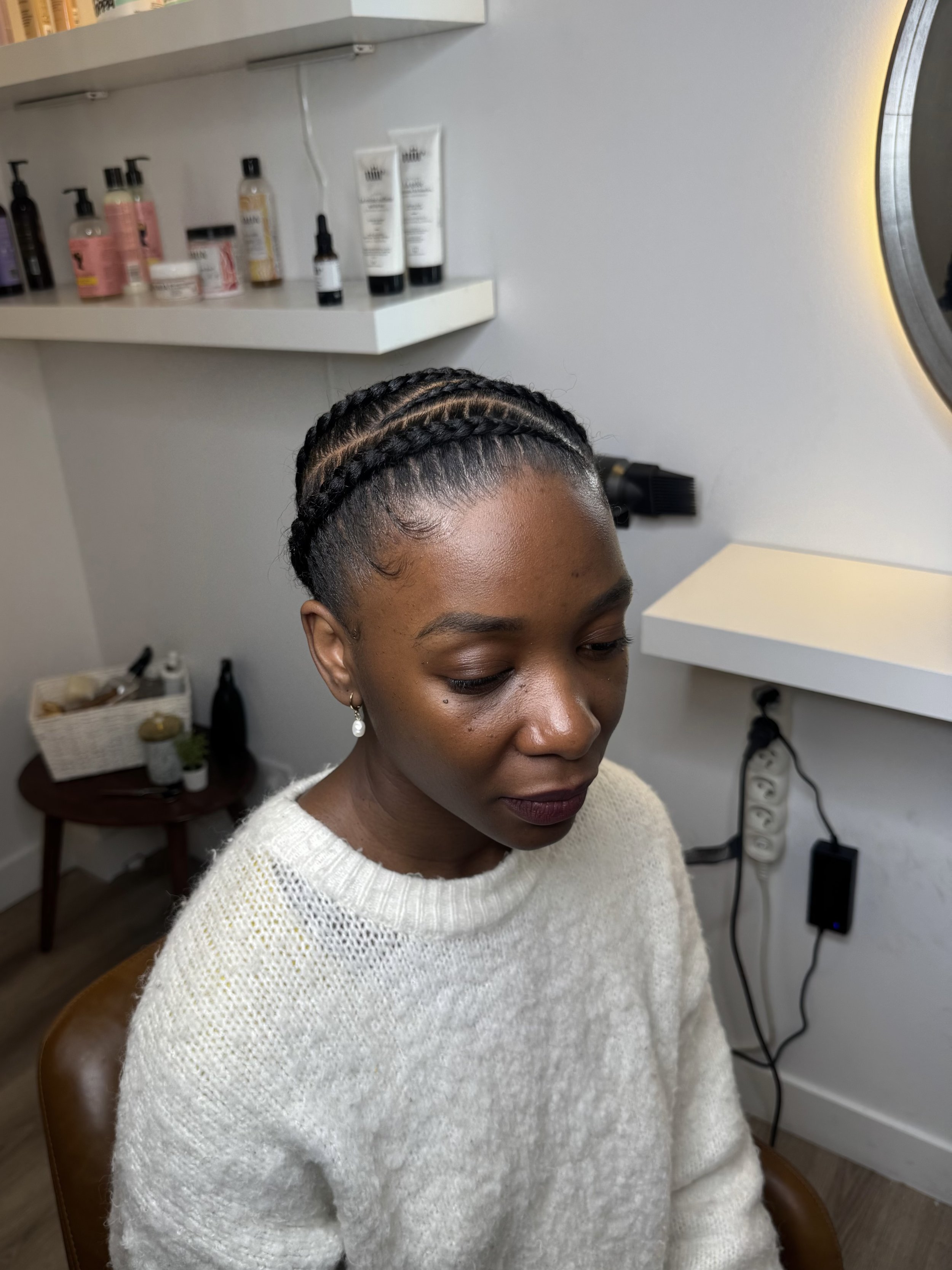 Une femme avec une coiffure à tresses assise dans un salon de coiffure, tresses sur cheveux naturels, cornrows sur cheveux naturels